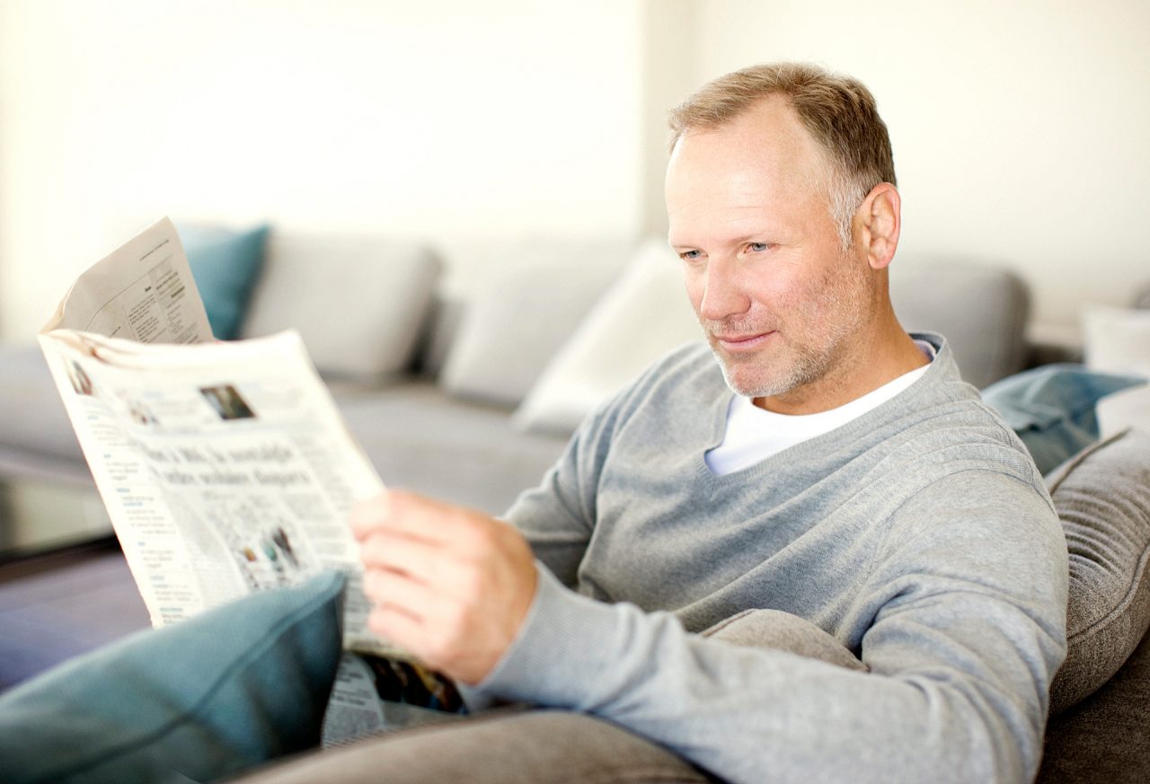 Man sitting on sofa reading newspaper