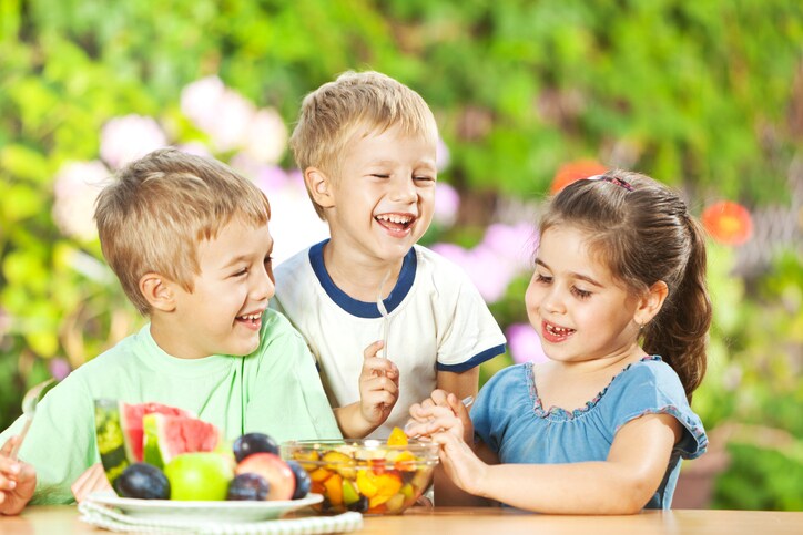 Group of small children having healthy snack, eating fresh fruit salad outdoors.