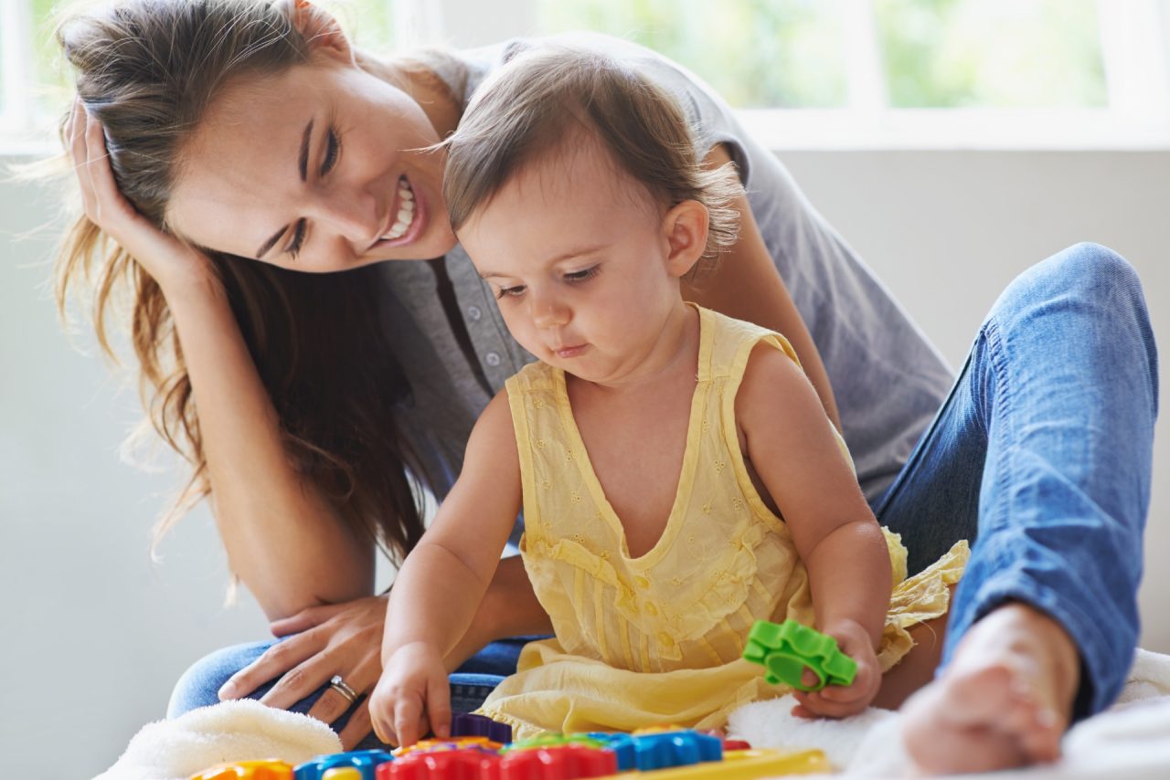 Shot of a cute baby girl sitting on the floor with her mom and playing with toys